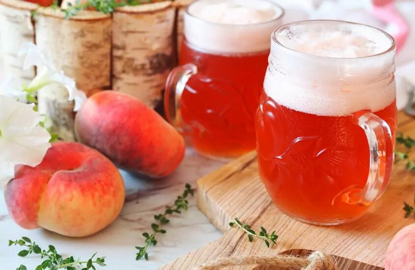 Glasses of Peach beer next to two peaches
