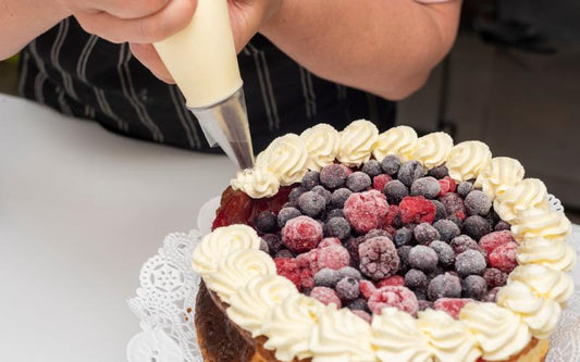 Baker adding frosting to a cake with different types of berries on top