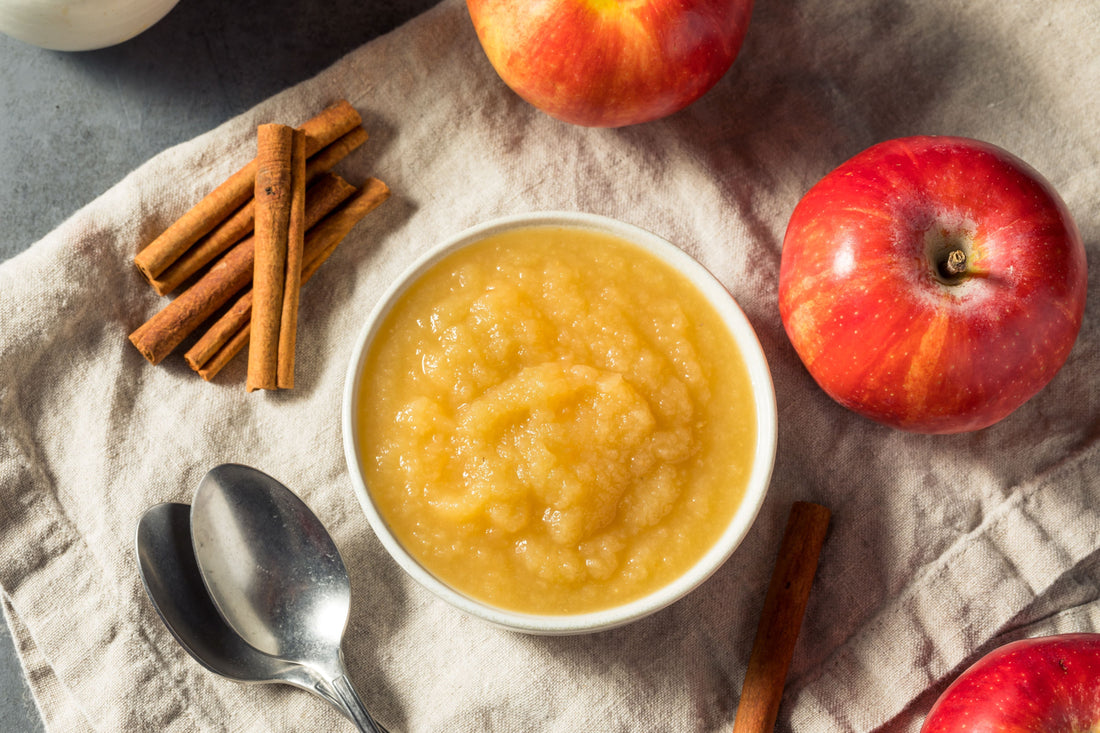 A bowl of apple compote surrounded by apples and cinnamon sticks