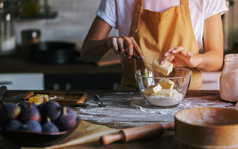 Margarine being cut into a bowl of flour to prepare a baked good