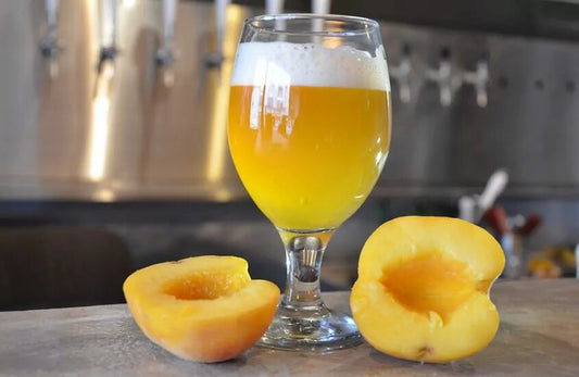 A glass of peach beer with two slices of peach by its side