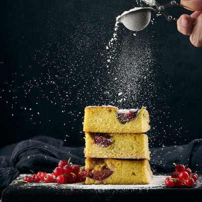 Three slices of Plum cakes stacked on top of each other while being dusted with powdered sugar