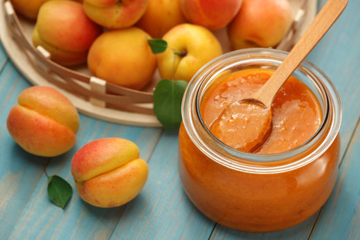 Jar of peach puree with a bowl of peaches in the background