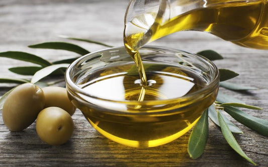 Oil being poured into a bowl next to three olives