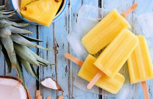 Four pineapple popsicles next to a slice of pineapple and a coconut