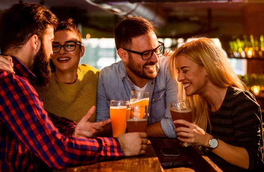 Friends sitting at a bar smiling with a glass of beer