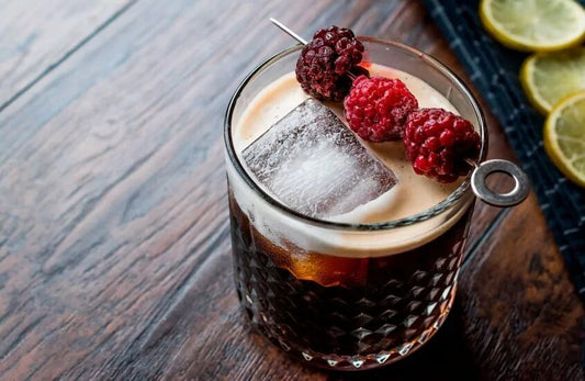 A cocktail with ice and raspberries sits on a table. 