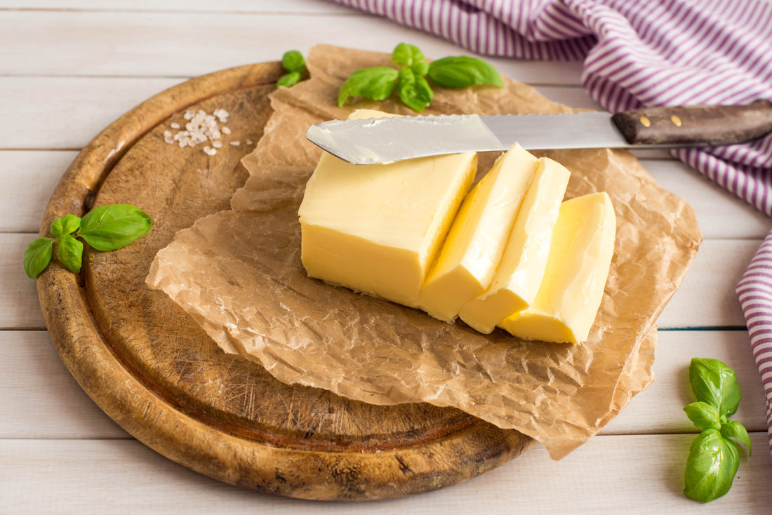 Cube of european butter cut into smaller slices in a cutting board with a knife on the side
