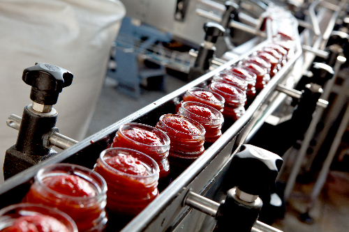 Food processing line where jars are being filled with a red sauce