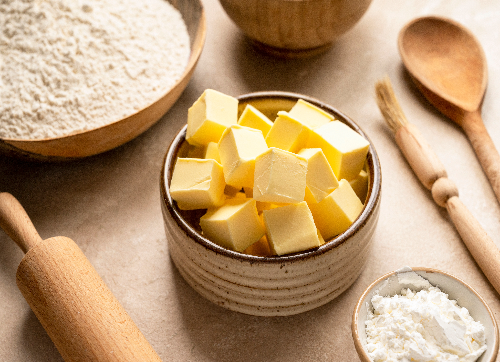 Cubed butter in a bowl next to flour and a rolling pin