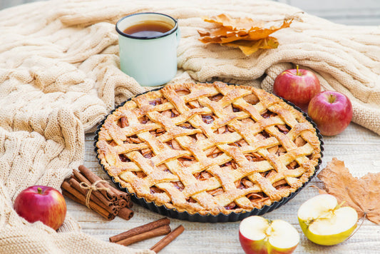 Apple pie surrounded by apples and cinnamon sticks 