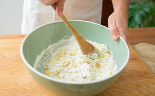 Bowl of flour with other bakery ingredients being mixed with a spoon spatula