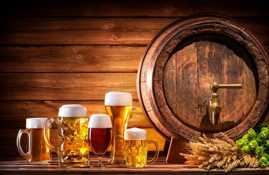 Variety of glasses with beer next to a beer barrel and hops